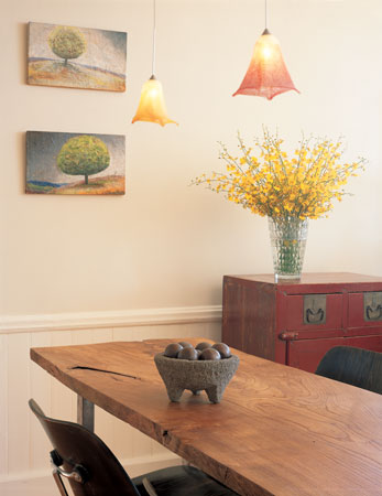 
Pendant lamps hand-blown from old vinegar bottles dangle above an elm-top table, creating a “dining zone” between the kitchen and living areas.
